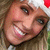A person with light brown hair wears a white and red Santa hat, smiling broadly in a pixelated close-up.