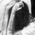 Black-and-white image of a person with long hair covering their face, viewed from above in three showing slight movement