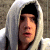 A pixelated close-up of a person wearing a light gray hooded garment with dark inner lining, set against a blurred background.