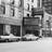 Black-and-white pixelated image showing a stylized building facade with rectangular windows and a central doorway, set against a textured background.