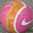 A pink and orange tennis ball with a white Nike swoosh logo on the right side, set against a gray pixelated background.