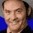 A pixelated image of a smiling man with short dark hair wearing a black shirt against a blue background, alongside text reading "ANCHORMAN" on a diagonal banner.