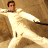 Pixelated figure in white outfit with arms extended, brown background, dark hair, and visible facial features.