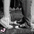 Pixelated grayscale image of a figure with dark hair and light clothing, partially obscured by motion blur or compression artifacts.
