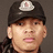 Pixelated close-up of a person wearing dark cap with white emblem, light skin tone, and visible ear.