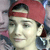 A pixelated close-up of a person wearing a red cap and dark clothing, with a blurred background.