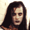 A person with long dark hair and pale makeup appears in three showing slight head movement, facial expression shifts, and a hand gesture