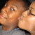 Two people in close proximity, one with eyes closed and lips puckered, the other with eyes open looking upward, all in a static image.