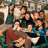 Group of people in various poses with visible clothing colors and background elements.