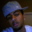 Pixelated image of a person wearing a blue cap and light blue shirt, with dark hair and a neutral expression against a dark background.