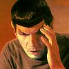A person with dark hair wearing a brown shirt, hand pressed against their forehead in a gesture of distress or fatigue.