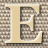 A static 48x48 pixel buddy icon featuring a large, stylized letter E in beige with dark brown and white shading against a checkered background.