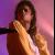 Pixelated image of a person holding a microphone against a purple and pink gradient background.