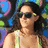 Pixelated image of a person with long dark hair wearing sunglasses and a light-colored sleeveless top against a colorful blurred background.