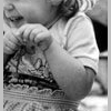 Black-and-white close-up of a child in a patterned dress with hands near the face, wearing a light short-sleeve shirt.