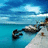 Pixelated beach scene with turquoise water, white sand, and a dark rocky outcrop under blue sky with light clouds.