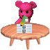 Pink pixelated bear with mouse ears holds green and yellow object over wooden table with striped item.