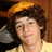 Pixelated image of a person with curly brown hair wearing an orange cap and light yellow shirt, set against a dark background with text overlays on bright yellow