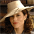 A pixelated close-up of a person wearing a light-colored wide-brimmed hat, brown hair, and red lips, with a blurred background.