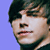 Pixelated close-up of a person's face with dark hair against a solid light blue background, showing partial facial features and clothing details.