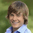 Pixelated portrait of a person with light brown hair and a light blue shirt against a green background.