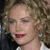 Pixelated close-up of a person with curly light brown hair, closed eyes, and red lips, wearing a white garment with a dark background.