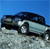 Pixelated image of a dark-colored car on a light surface under a blue sky background.