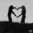 Two silhouetted figures form a heart shape with their arms against a light background, standing on a dark horizontal base.