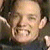 Pixelated close-up of a person's face with closed eyes, light skin tone, and visible ear, set against a dark background with indistinct shapes.