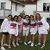 Group of seven people in white shirts with red and pink graphics standing on grass near a building.