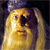 A pixelated yellow figure with a dark brown face and black eyes, wearing a blue cap, against a dark background.