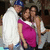 Three people pose together in a group photo with one person wearing a blue cap and white shirt, another in a pink top, and the third in light-colored clothing.