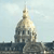 Pixelated image of a large domed building with a spire against a light blue sky, showing architectural details and surrounding structures.
