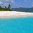 A beach scene with white sand, turquoise water, and green trees under a blue sky with scattered clouds.