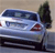 A light blue sedan with dark blue roof and red taillights is positioned on a road, viewed from the rear three-quarter angle with a tree in the background.