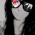 A person with long dark hair wears black sunglasses reflecting a red and white pattern, positioned against a light background.