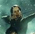 Pixelated image of a person with light brown hair wearing a dark long-sleeve top, arms extended horizontally against a teal background.