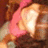 Pixelated image of a light-colored figure with a pink accessory against a brown background.