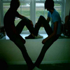Two silhouetted figures sit on a windowsill, legs extended to form a heart shape against a bright window background.