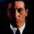 Pixelated static image of a person with light skin tone wearing dark clothing and white collar, set against black background.