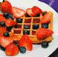 A waffle topped with strawberries and blueberries on a white plate, next to text reading "Waffles Is Good" in pixelated font.