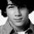 Black-and-white portrait of a person with dark hair and a collared shirt, displayed in a with visible pixelation