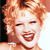 Pixelated close-up of a person with curly light brown hair, red lips, and a wide open mouth showing teeth, set against a dark and light background.