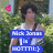 Pixelated image of a person with dark hair wearing a white sleeveless top, holding blue signs with partially readable text against a green foliage background.