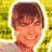 Pixelated static image of a person with brown hair and light skin smiling, set against a yellow-green patterned background.