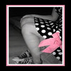 A grayscale figure with a pink bow and polka-dot dress, framed by a pink border, viewed from a low angle.