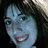 A pixelated image of a person with brown hair and a light-colored headband, smiling with visible teeth, with green text reading 'Anne Safron' overlaid on the right side.
