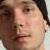 Static pixelated close-up of a person's face with dark hair, light skin, and visible facial features including eyes, nose, and mouth.