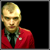 A person in a red blazer and black tie appears in a of with changing text overlays on a black background