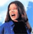 A pixelated image of a person with long dark hair wearing a blue and black top against a light blue background.